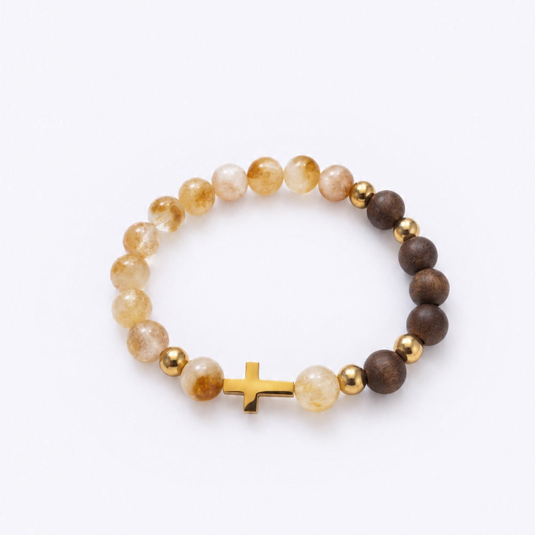 A beaded stretch bracelet featuring translucent yellow and brown beads, polished gold spacer beads, and a small gold cross charm, displayed on a clean white background.