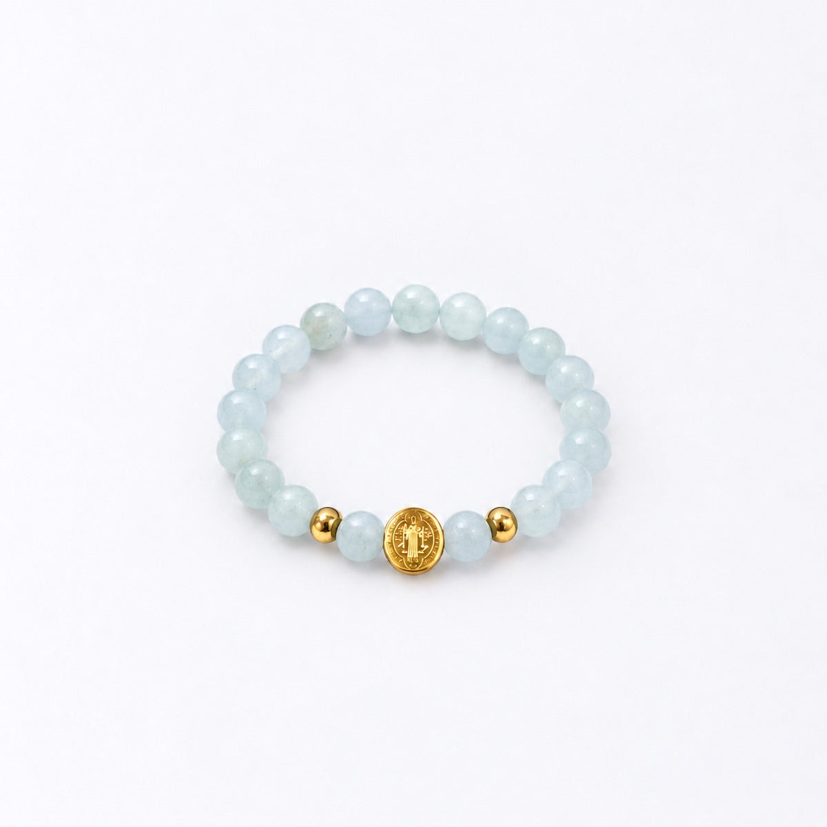 A beaded stretch bracelet featuring light blue-green round beads, two small gold spacer beads, and a central gold round charm with a St Benedict symbol, displayed on a clean white background.