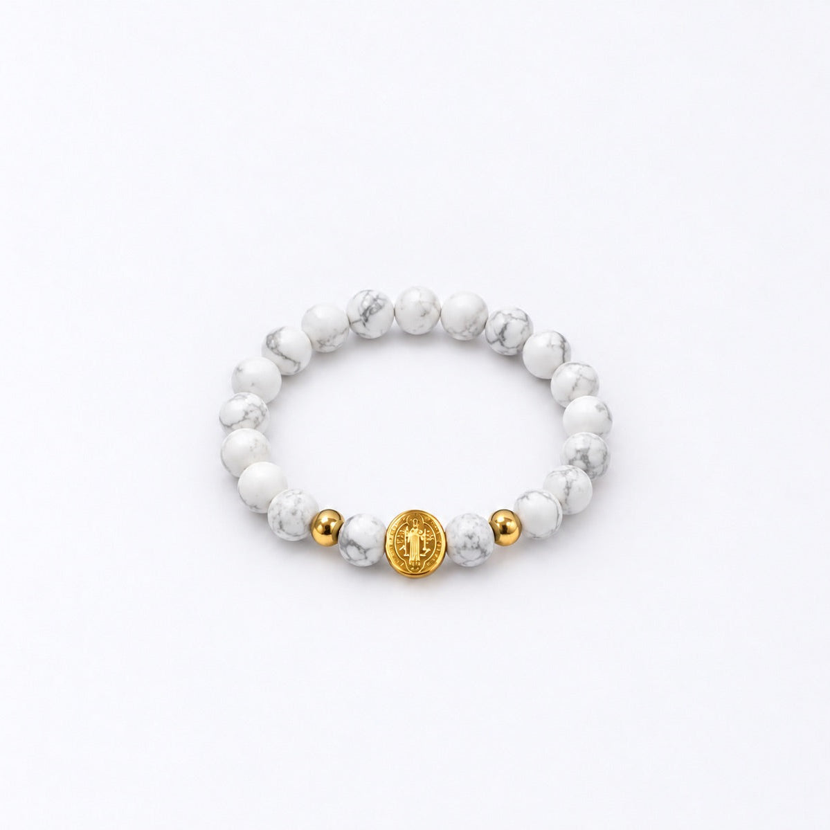 A beaded stretch bracelet featuring white and gray marbled round beads, accented by two small gold spacer beads and a larger central gold disc charm with an St Benedict symbol, shown on a clean white background.