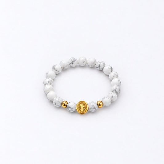 A beaded stretch bracelet featuring white and gray marbled round beads, accented by two small gold spacer beads and a larger central gold disc charm with an St Benedict symbol, shown on a clean white background.