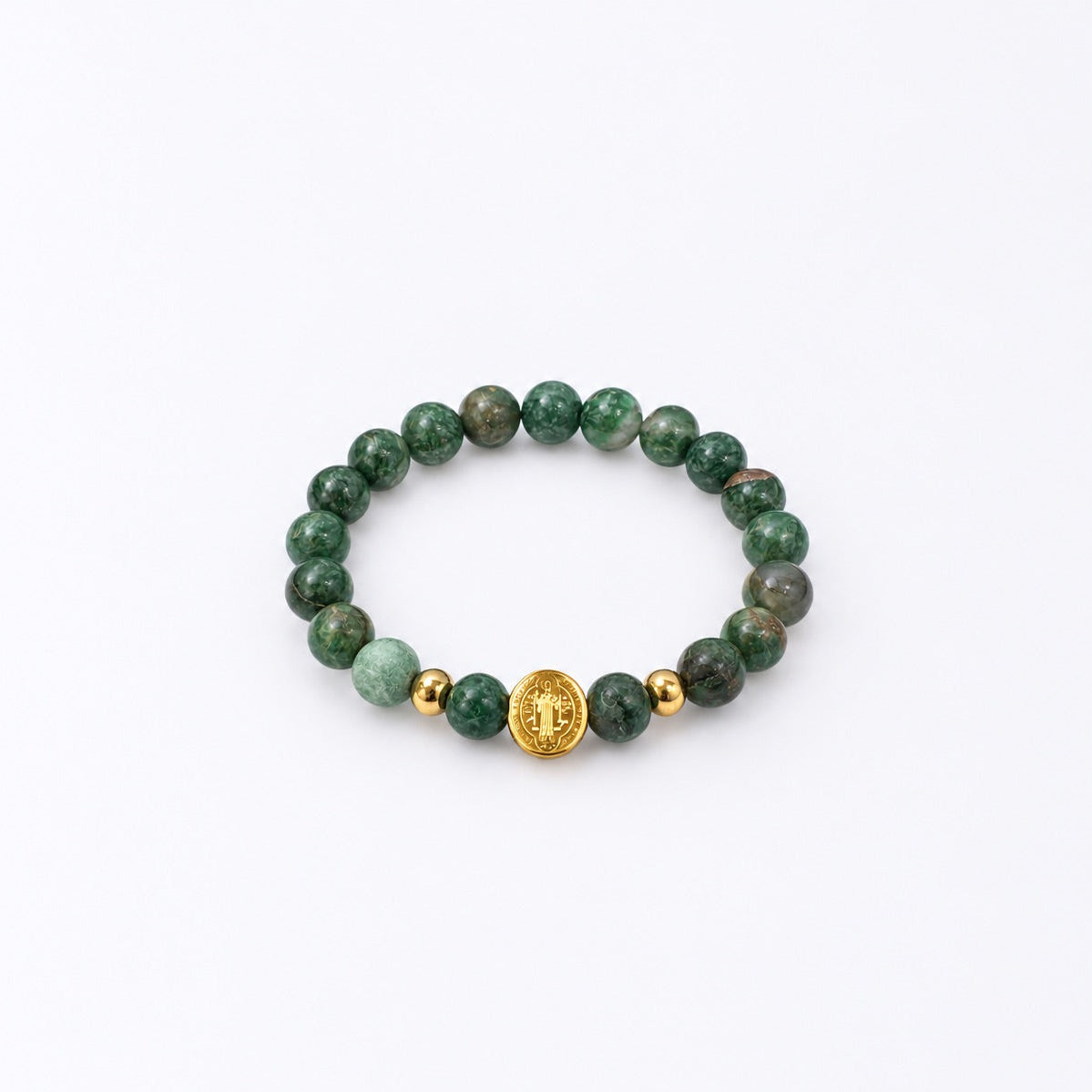 A beaded stretch bracelet featuring round green stone beads, a light green marble bead, two small gold spacer beads, and a central gold oval charm with a St Benedict symbol, displayed on a clean white background.